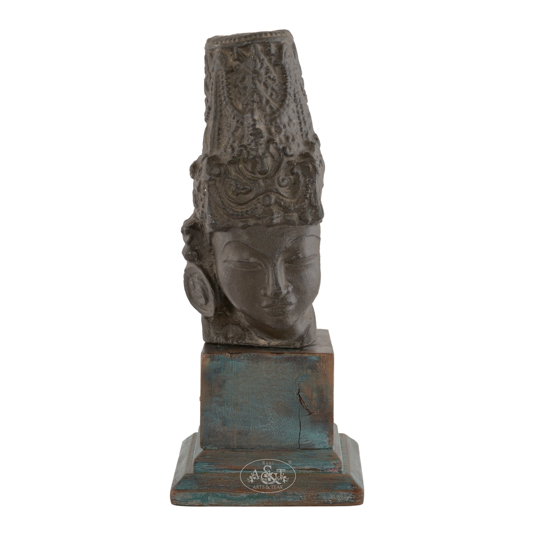 Antique brass head sculpture with a stand, featuring intricate detailing on the crown, set against a distressed teal wooden base.