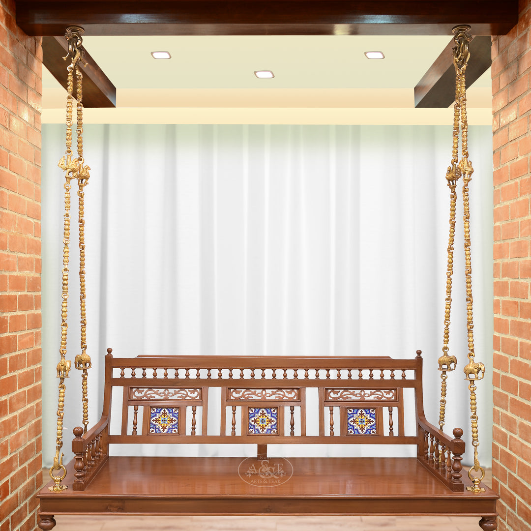Wooden swing with decorative backrest against a white curtain and brick wall.
